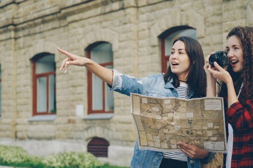 Two people examining a map outdoors with a stone building in the background. 1