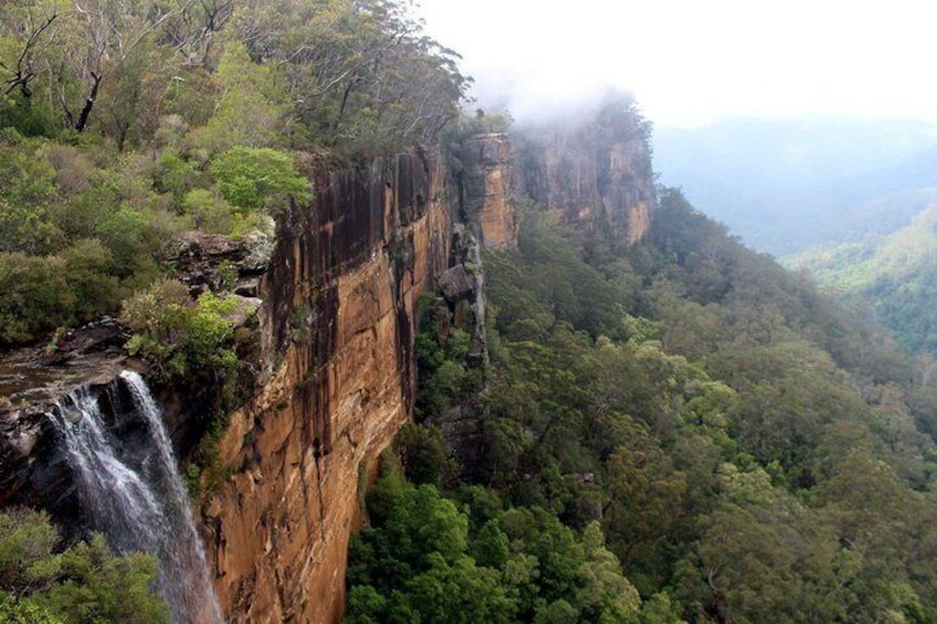 A waterfall cascading down a steep cliff surrounded by dense forest. 2