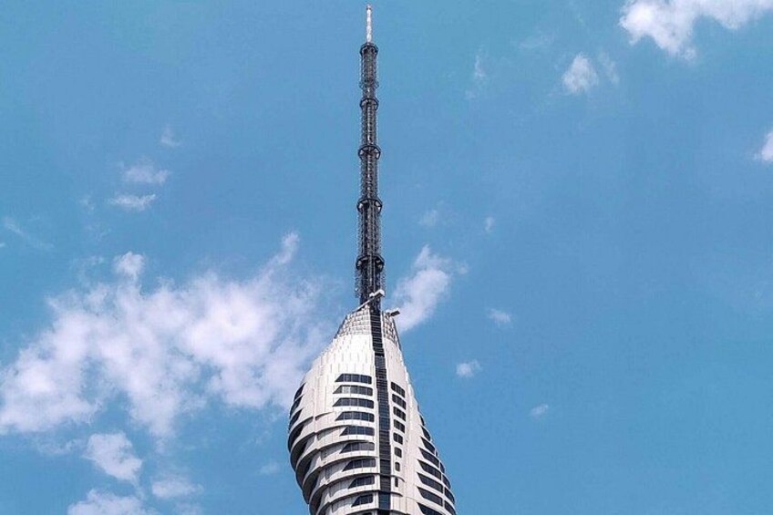 A tall building with a pointed top and a cylindrical base, against a clear blue sky with scattered clouds. 1