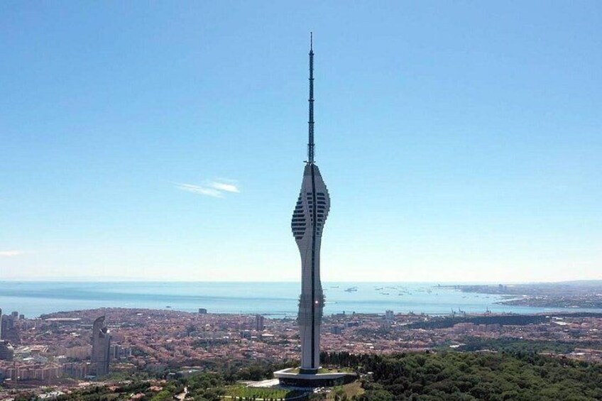 A tall, slender tower with a unique design, surrounded by a cityscape and a body of water in the background. 2