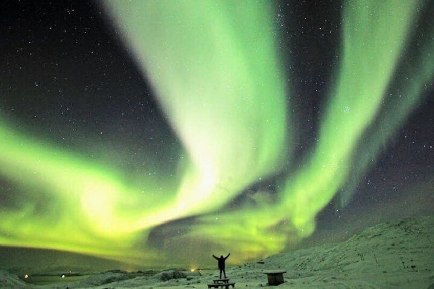 The Northern Lights over a snowy landscape with a person standing in the foreground. 4