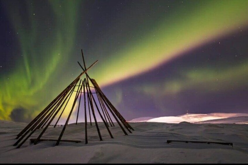 A snow-covered landscape with a wooden structure resembling a teepee under a vibrant northern lights display. 5