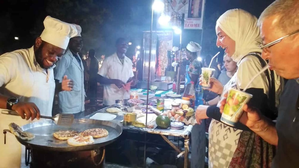 A street food vendor cooking on a large flat griddle, with various food items and condiments visible. 4