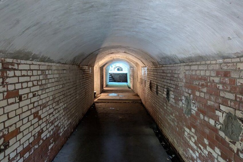 A brick-lined tunnel with a concrete ceiling and a small window at the end. 3