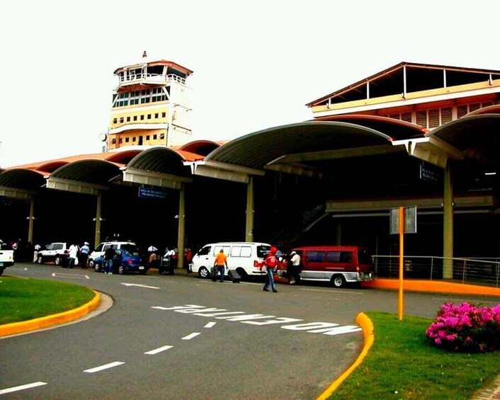 A parking lot with vehicles, a building with a tower, and a covered walkway. 2