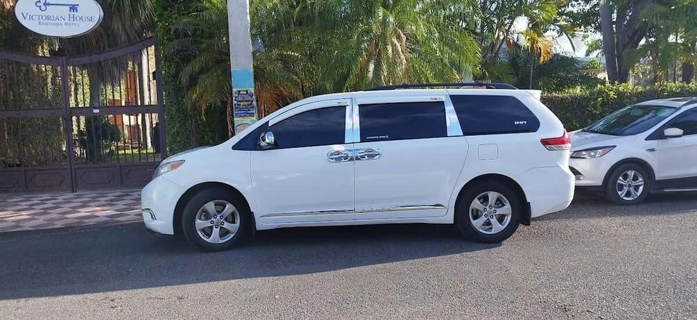 A white minivan parked on a street with a gated entrance and palm trees in the background. 3
