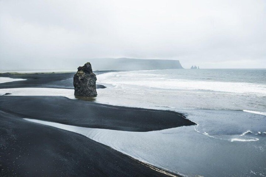 A rock formation on a beach with a calm sea and distant cliffs. 5