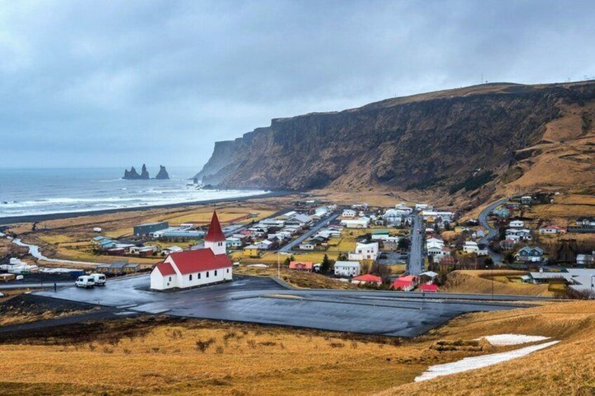 A coastal town with a prominent red-roofed church, a rugged coastline, and a mountainous backdrop. 1