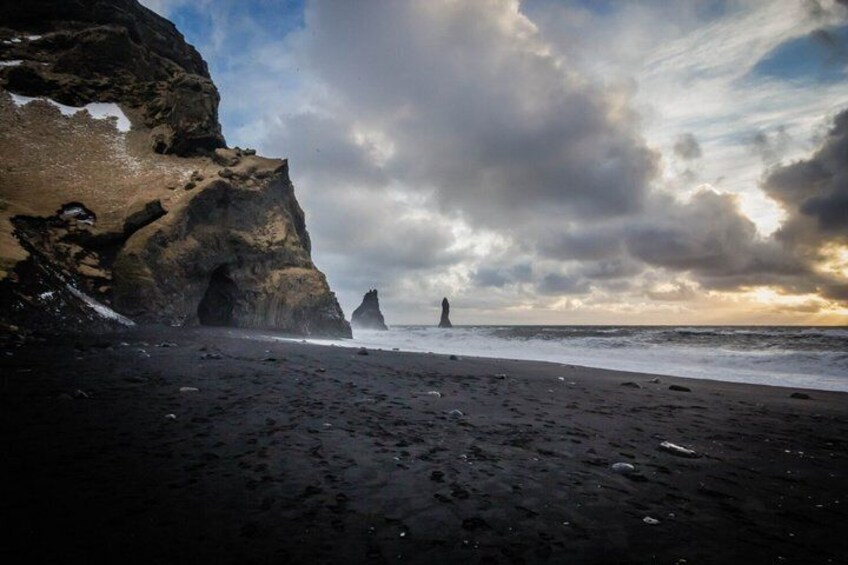 A rocky coastline with a large cave-like formation and a distant rock pillar. 3