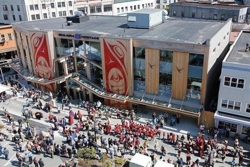A crowded public square with a modern building featuring large red banners. 4