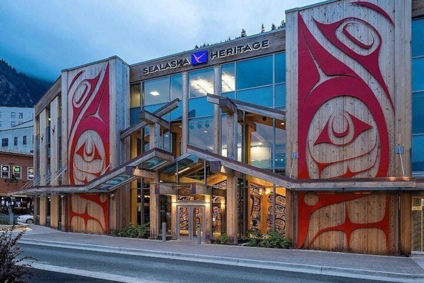 A building with large indigenous artwork on its facade, a glass entrance, and the name 'SEALASKA HERITAGE' on the top. 2