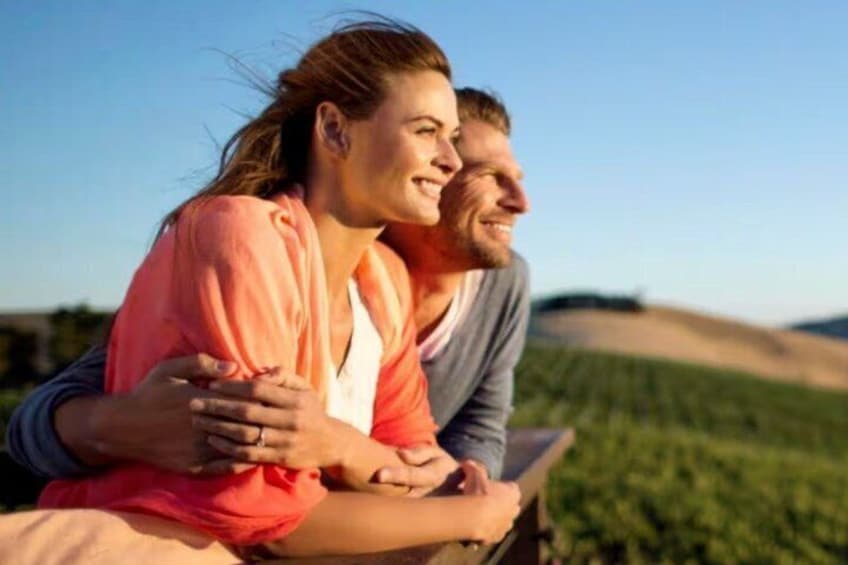 A couple sitting on a bench in a field with a clear sky. 4