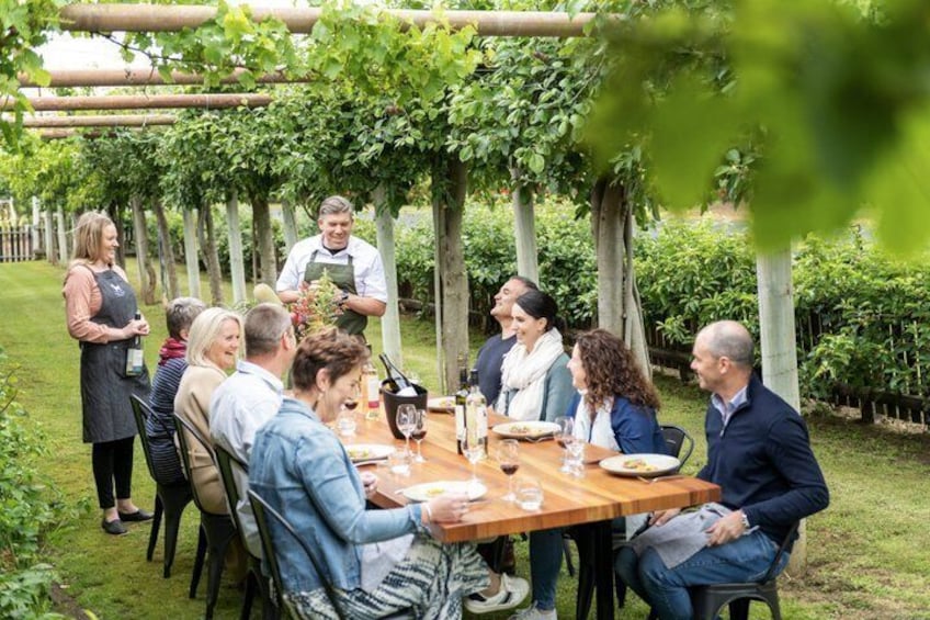 A group of people dining outdoors under a pergola with a wooden table and chairs. 3