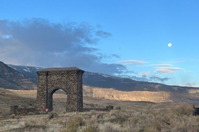Un arco de piedra en un campo cubierto de hierba, con montañas al fondo. 5