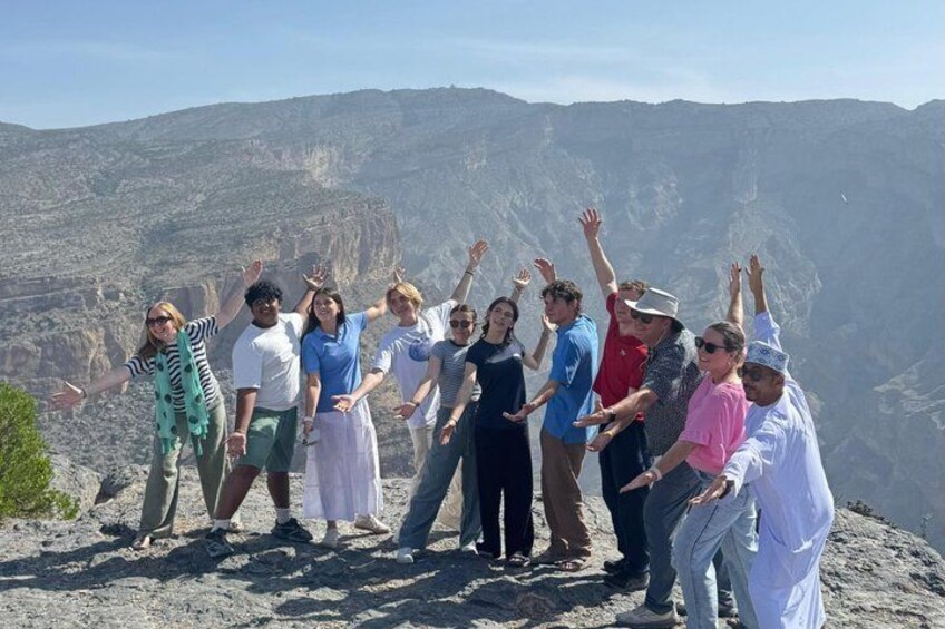 A group of people standing on a rocky outcrop with their arms raised, overlooking a mountainous landscape. 4