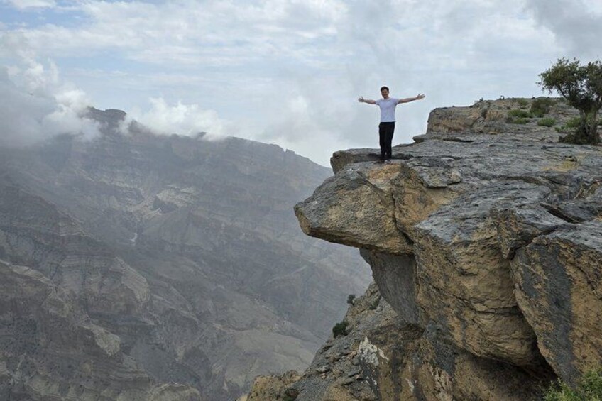 A person standing on a rock outcrop with arms outstretched, overlooking a mountainous landscape. 1