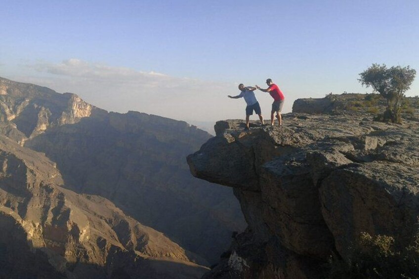 Two people standing on a rocky cliff edge with a canyon in the background. 3