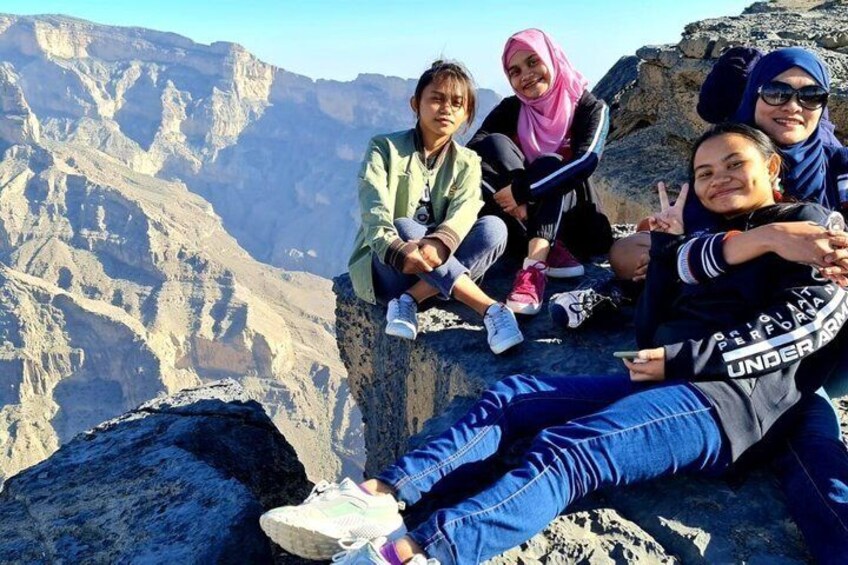 A group of people sitting on a rocky ledge with a mountainous landscape in the background. 5