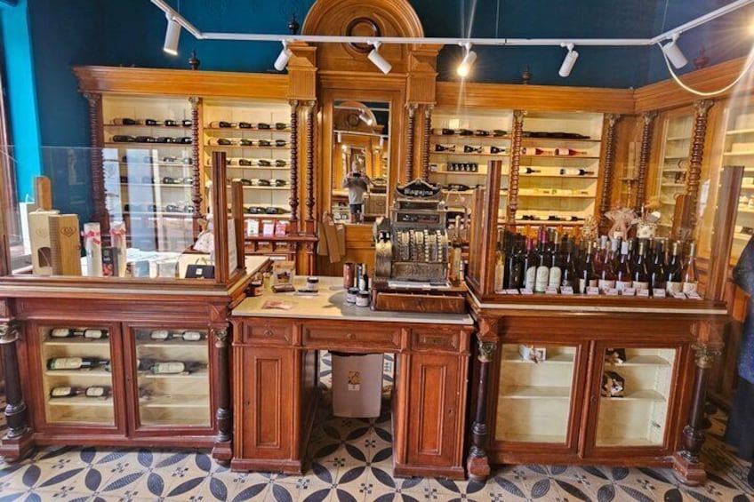 A vintage wine shop with wooden shelves and cabinets, and a patterned floor. 3