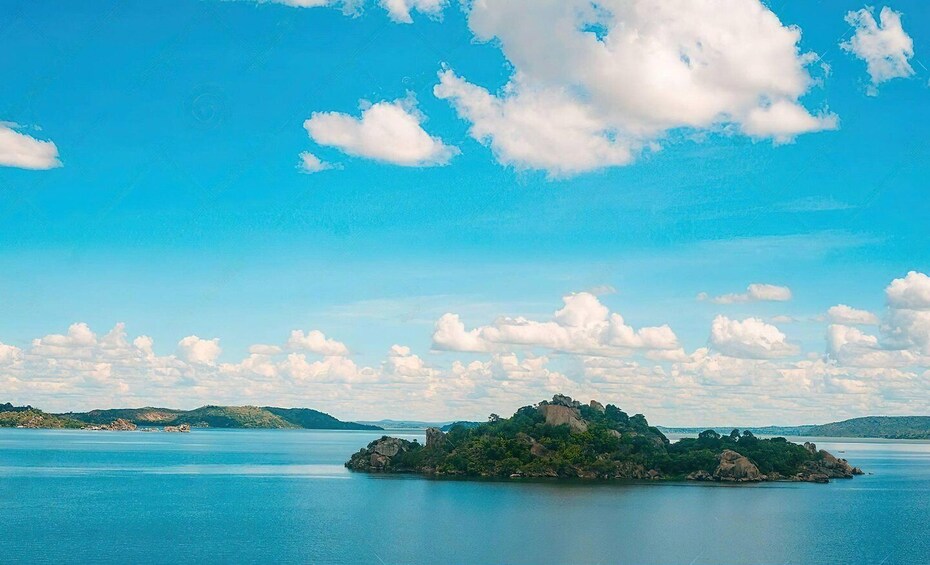 A calm lake with a small island covered in greenery and rocks. 1