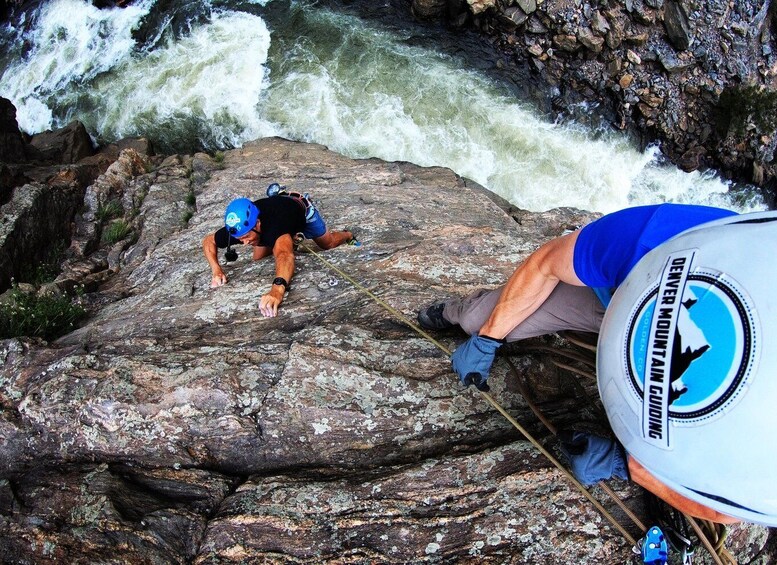 A person rappelling down a rocky cliff with a river in the background. 1