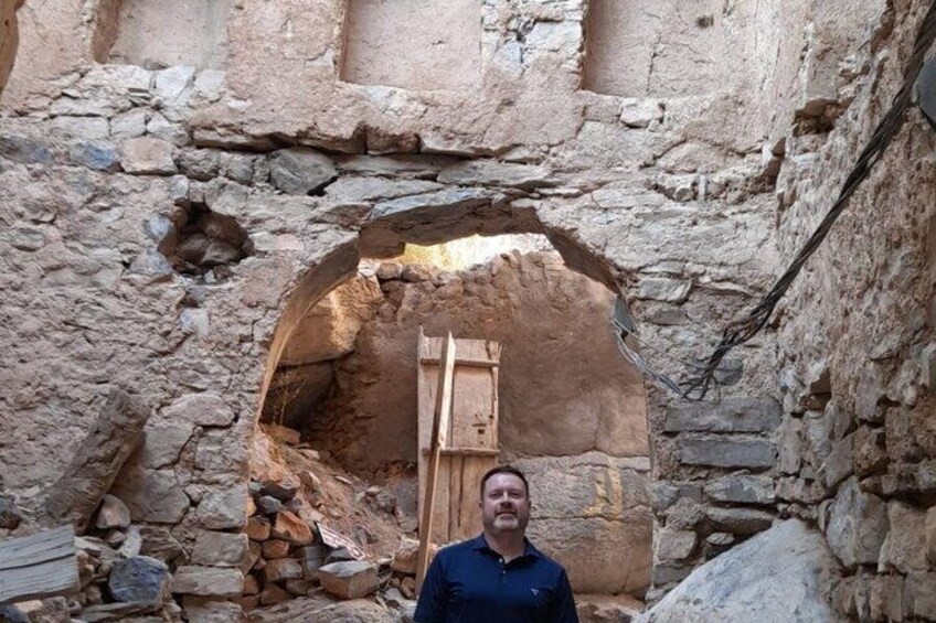 A man standing in front of an ancient stone structure with a wooden ladder leaning against it. 2