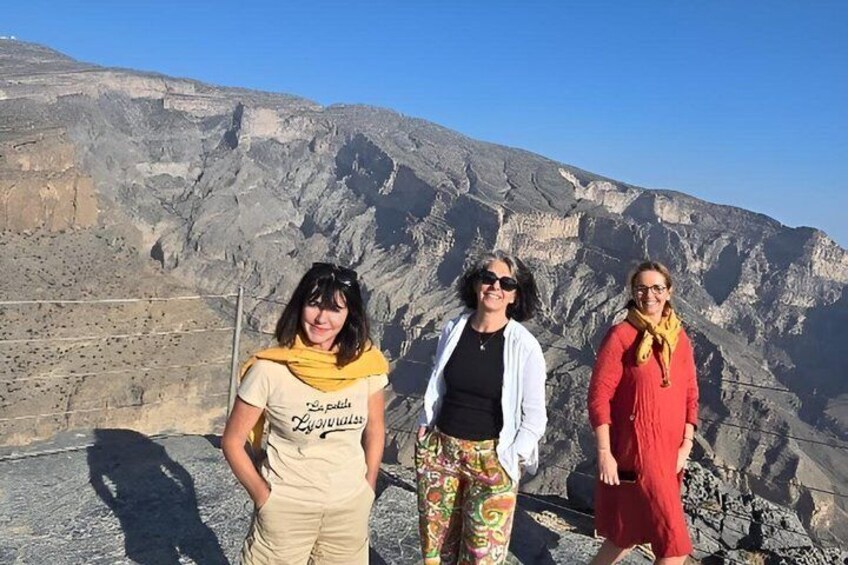 Three people standing on a rocky outcrop with a mountainous landscape in the background. 1