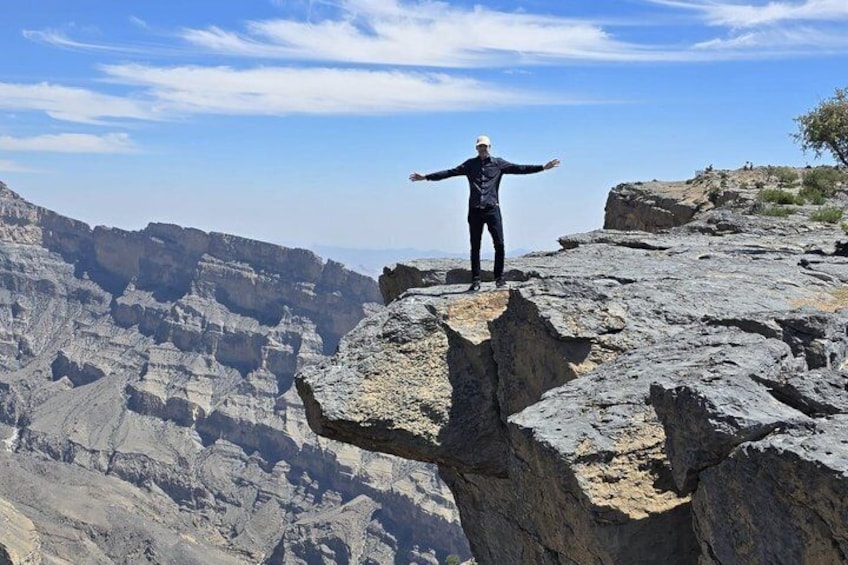 A person standing on a rocky cliff with arms outstretched, overlooking a vast canyon landscape. 5