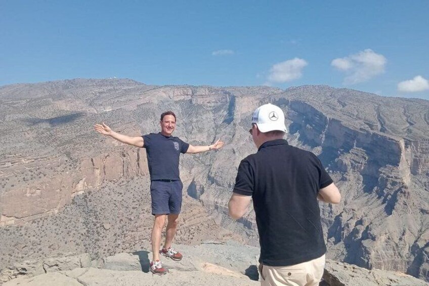 Two people standing on a rocky outcrop with a vast canyon in the background. 4