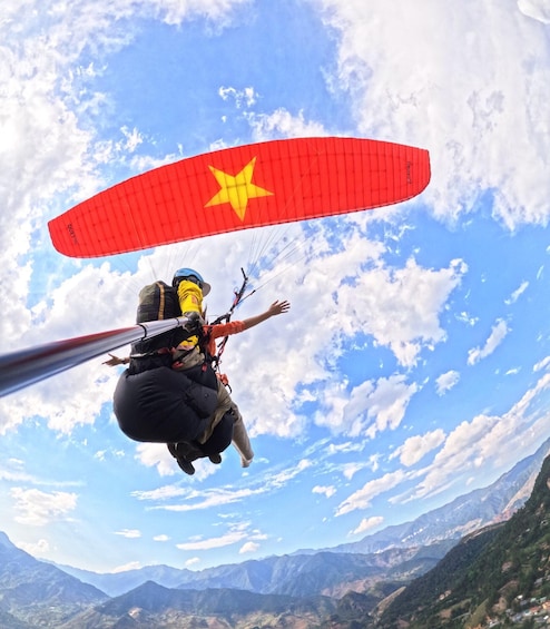 A person paragliding with a red parachute featuring a yellow star, against a backdrop of a clear sky and mountainous terrain. 5