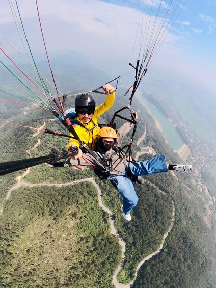 Two people paragliding over a mountainous landscape with roads and a body of water visible below. 4