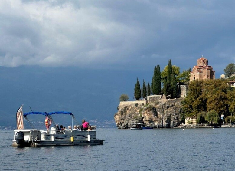 A boat on calm water, a rocky cliff with a church, and a clear sky. 5