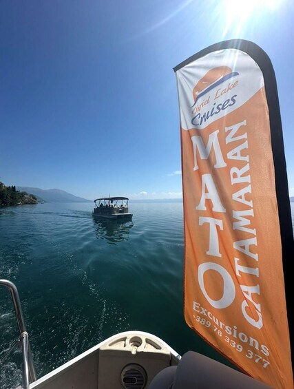 A boat with a banner advertising 'Mato Catamaran Excursions' on a calm lake with a clear sky. 3