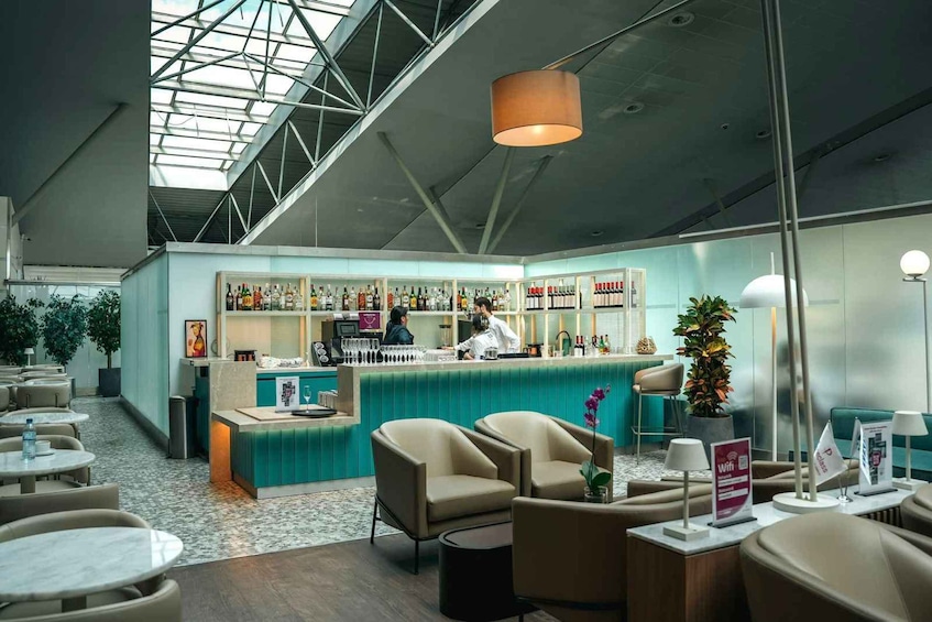 A modern bar area with a high ceiling and skylight, featuring a bar counter, seating, and a variety of bottles. 4