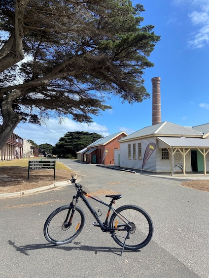 A bicycle parked on a street, a signpost with directions, a large tree, and a building with a chimney. 2