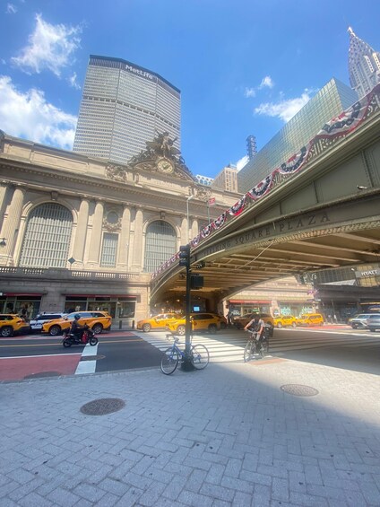 A busy urban street with a historic train station, yellow taxis, and a cyclist. 2