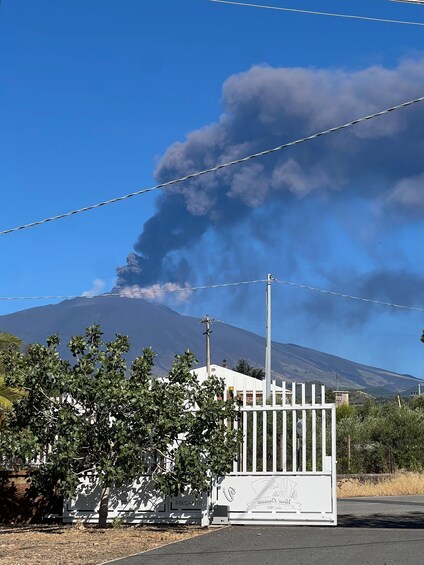 A white building with graffiti, a fence, and a mountain with smoke in the background. 3