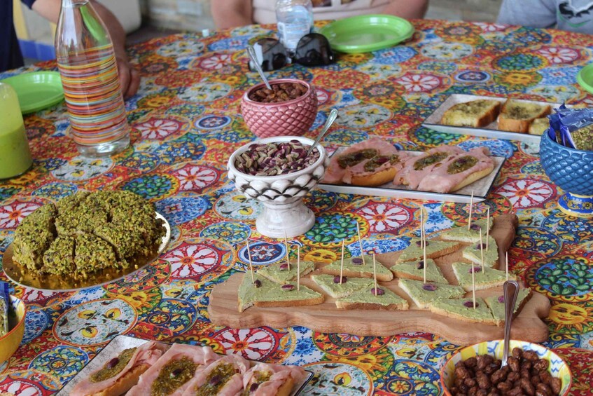 A table with various food items, including a dish with green toppings, a bowl of nuts, and several types of bread. 5