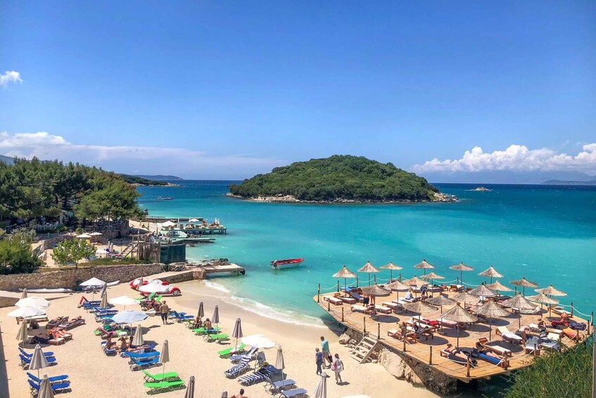 A beach with sun loungers, umbrellas, and a small island in the distance. 1