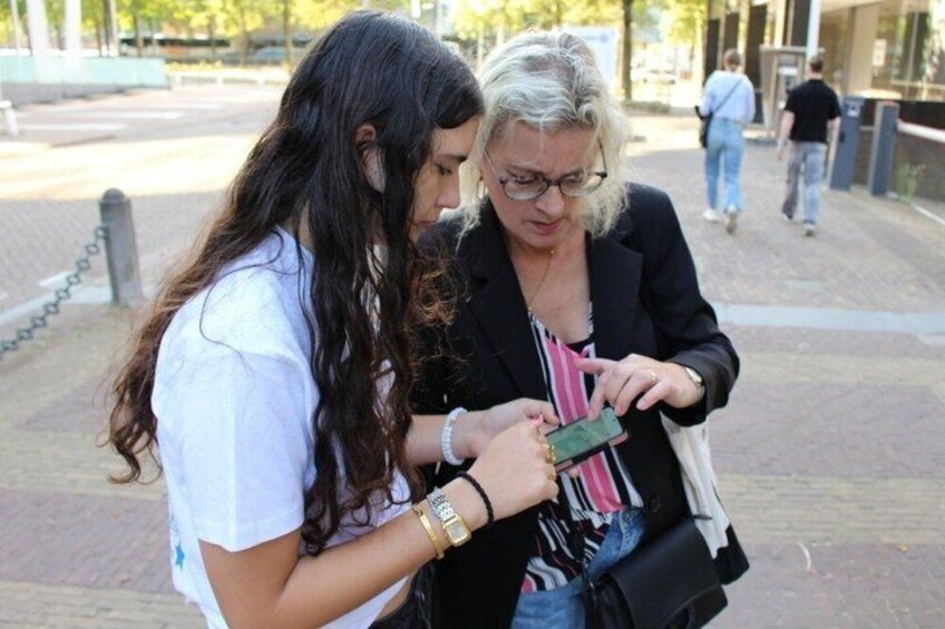 Two people examining a green device, possibly a smartphone, outdoors with a paved walkway and a building in the background. 5