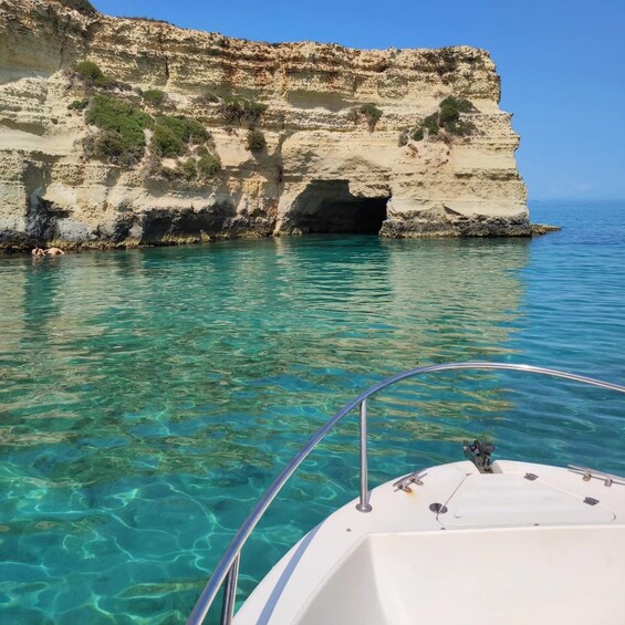 A boat near a rocky coastline with clear turquoise water and a cave entrance. 4