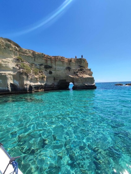 A coastal landscape with clear turquoise waters, a rocky cliff, and a small cave entrance. 5