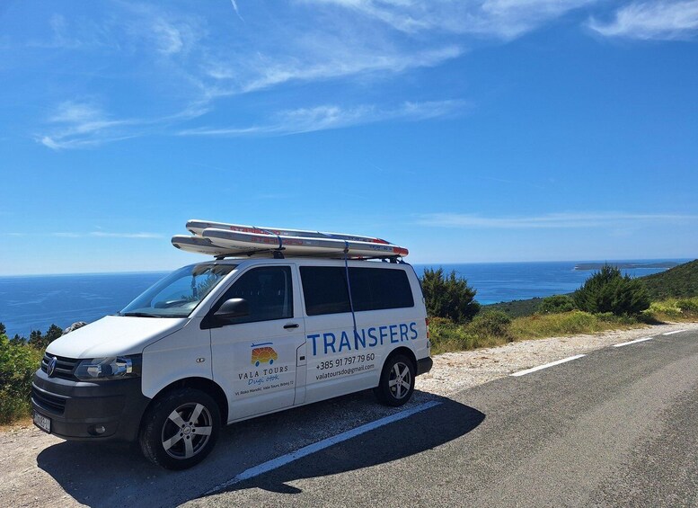 A white van with surfboards on the roof parked on a road with a coastal view. 2