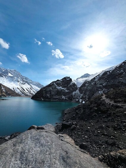 A mountainous landscape with a turquoise lake, rocky terrain, and snow-capped peaks under a clear sky. 1