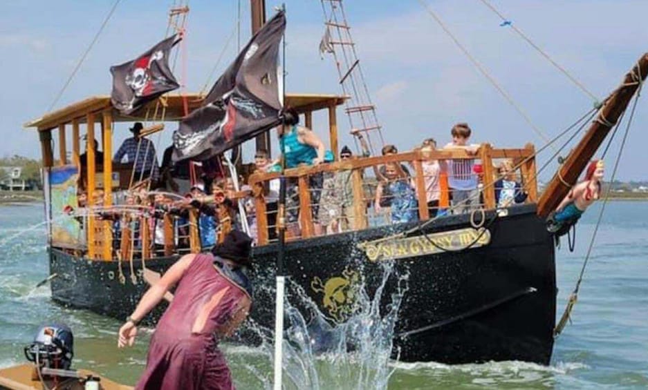 A pirate-themed boat with people on board, a black hull, and a flag with a skull and crossbones. 3