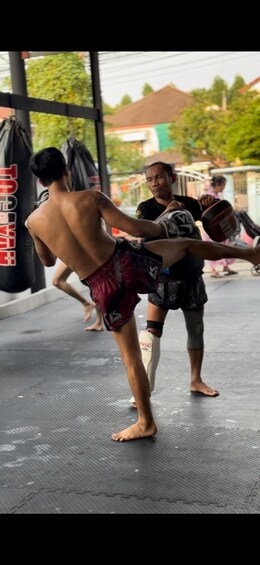 A person practicing martial arts, wearing red shorts, on a mat with a punching bag in the background. 4
