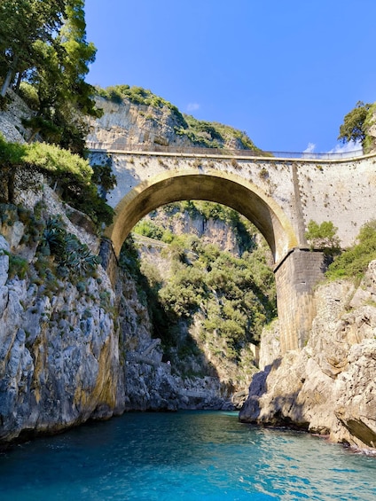 A stone bridge over a river, surrounded by rocky cliffs and greenery. 2