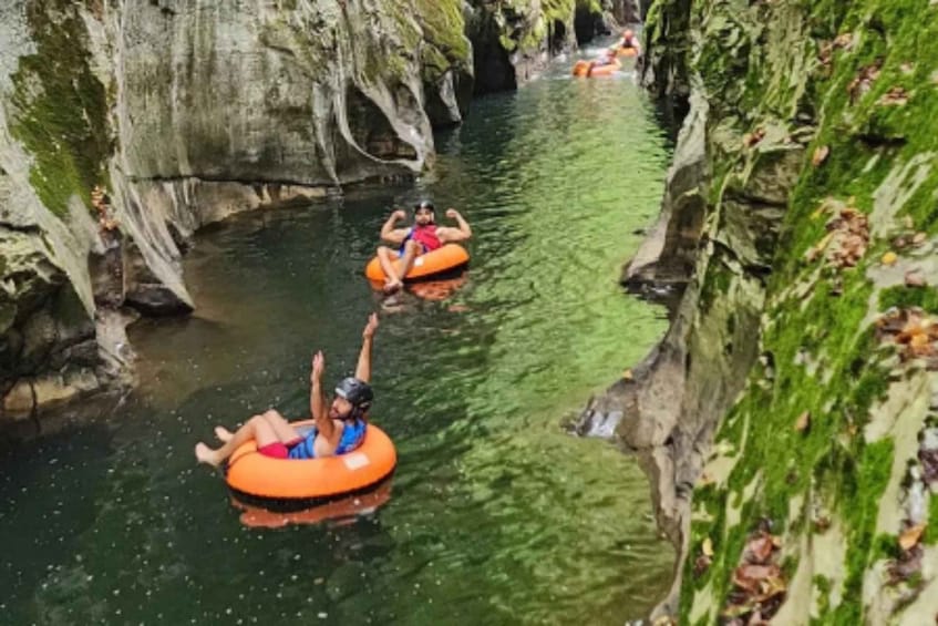 People floating on an orange tube in a narrow water channel surrounded by rocky cliffs. 3