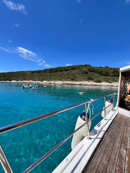 A boat on clear turquoise water with a rocky shoreline and a forested hill in the background. 2