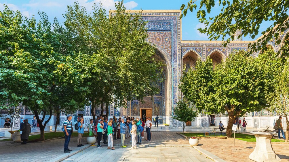 A courtyard with a large, intricately tiled building, surrounded by trees and people. 2